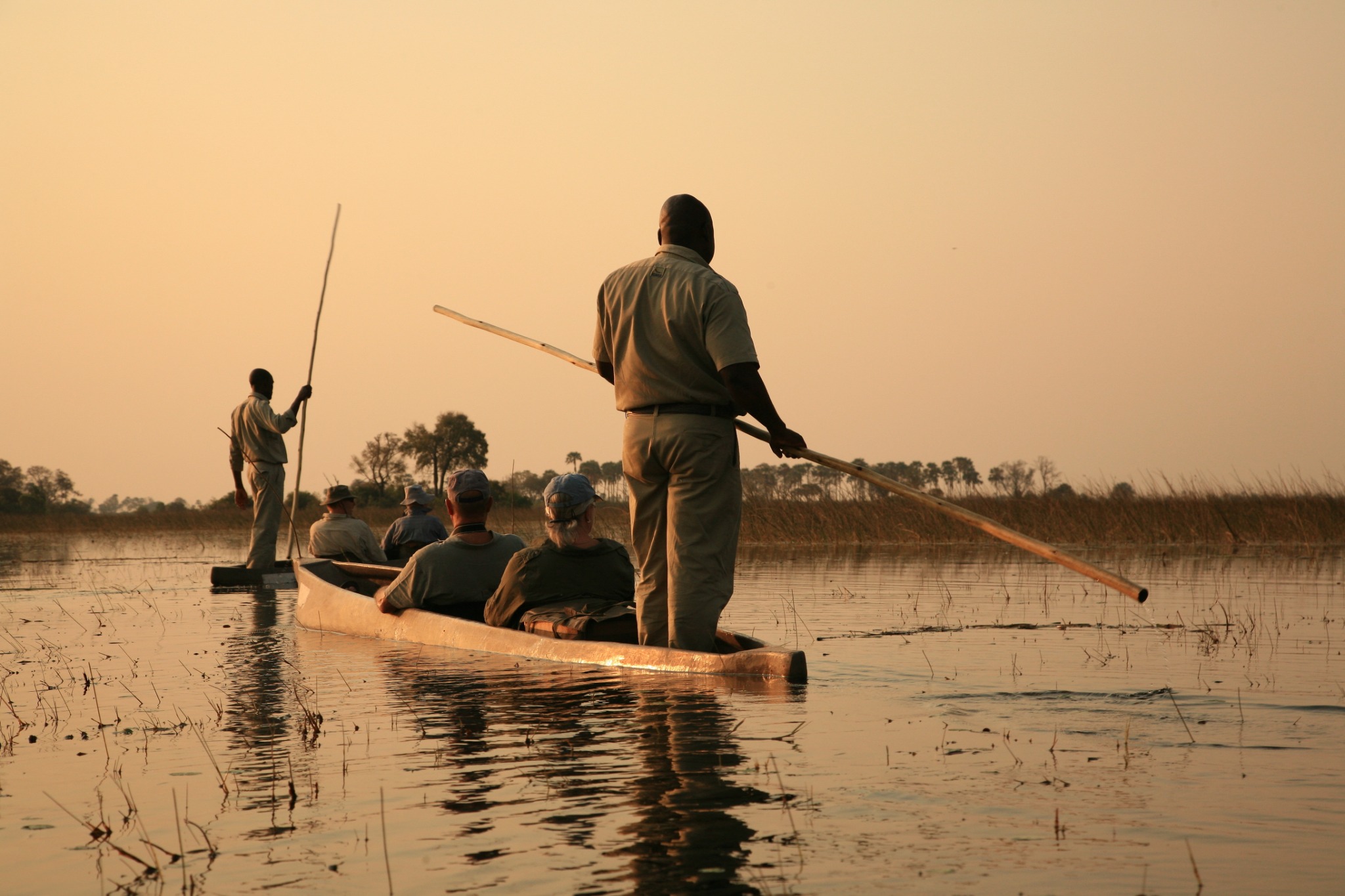 Viajeros recorriendo en mokoro el delta del Okavango al atardecer